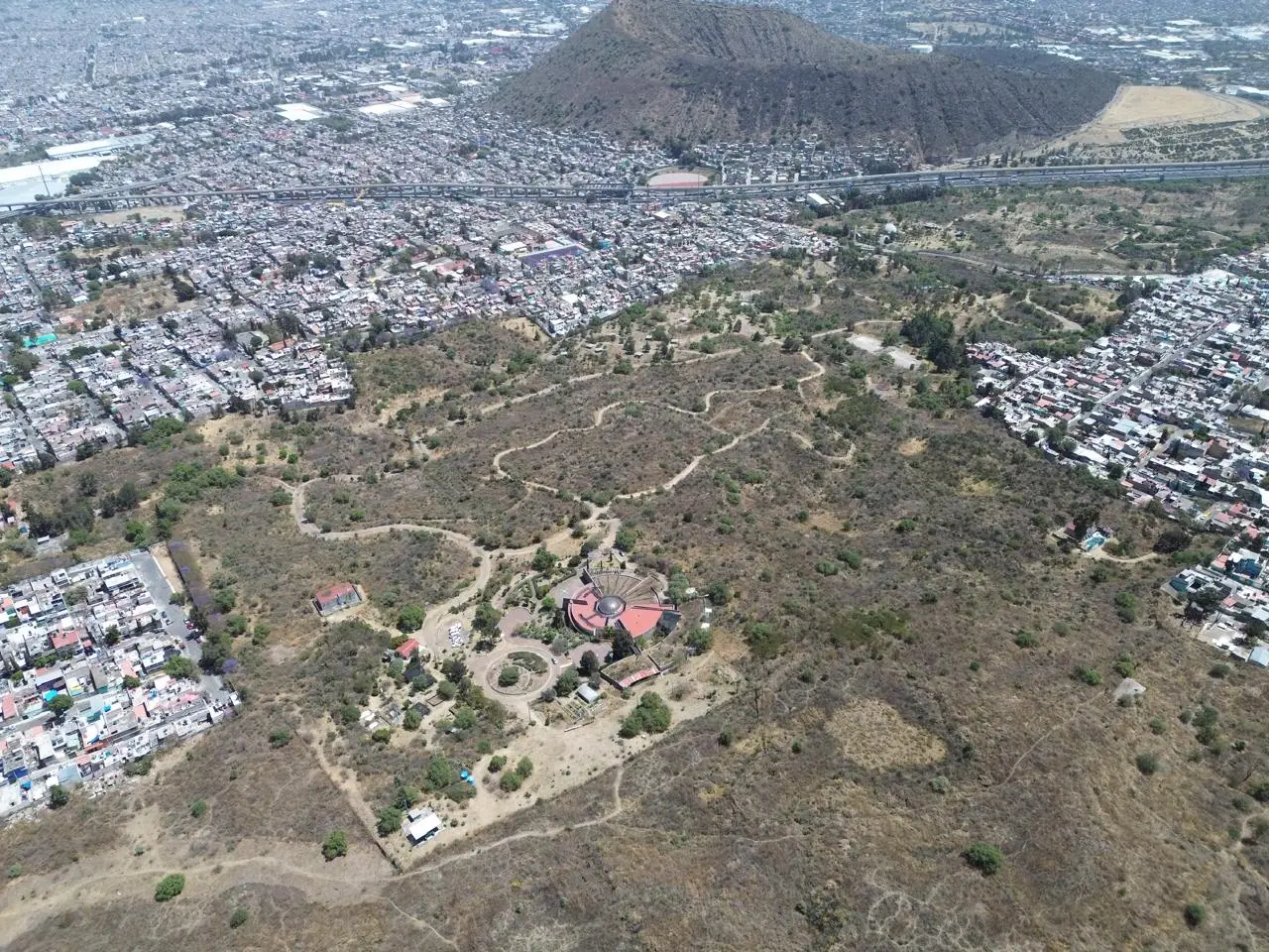 Vista aérea de un paisaje con vegetación, senderos y zonas urbanas alrededor.